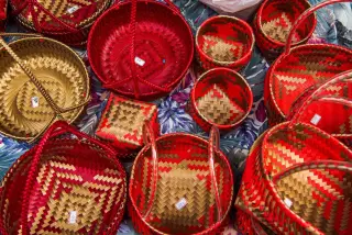 Ilustrasi: Deretan keranjang anyaman berwarna merah dan emas dengan label harga di atas kain bermotif.