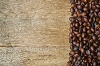 Ilustrasi: Biji kopi sangrai berjajar di sisi kanan permukaan meja kayu.