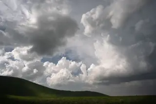 Ilustrasi: Pemandangan bukit hijau dengan hamparan langit berawan tebal.