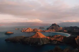 Ilustrasi: Pemandangan perbukitan pulau dan teluk laut di perairan tropis saat senja.
