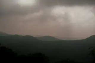 Ilustrasi: Pemandangan deretan bukit hijau di bawah langit mendung gelap berawan tebal.