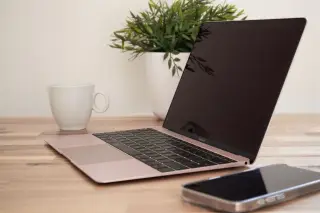 Ilustrasi: Laptop terbuka, cangkir putih, ponsel, dan tanaman hias di atas meja kayu.