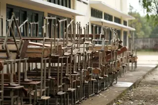 Ilustrasi: Tumpukan meja dan kursi sekolah usang di luar gedung sekolah.