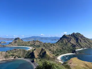 Ilustrasi: Pemandangan lanskap perbukitan Pulau Padar dengan teluk berpasir putih dan laut biru.