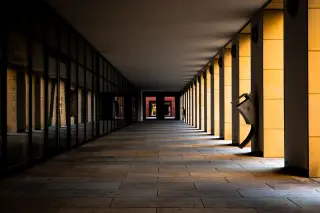 Ilustrasi: Lorong panjang sebuah gedung modern yang sepi dengan deretan pilar dan pencahayaan alami.