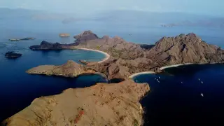 Pemandangan udara menunjukkan pulau berbukit dengan beberapa teluk berpasir dan perahu-perahu di perairan biru. Pulau Padar, Selasa (22/9/2026).