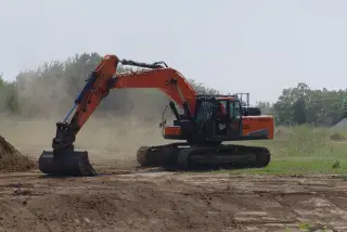 Ilustrasi: Sebuah eskavator berwarna jingga sedang mengeruk tanah di area proyek terbuka.