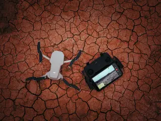 Ilustrasi: Sebuah drone dan pengendali jarak jauh tergeletak di atas tanah kering yang retak-retak.