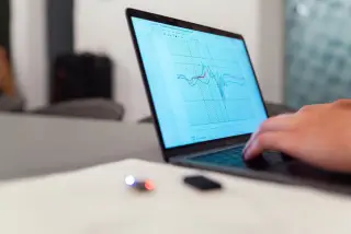 Ilustrasi: Tangan seseorang mengetik di laptop yang menampilkan grafik data seismik atau analitik.