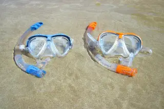 Ilustrasi: Dua set masker selam dan snorkel diletakkan di atas pasir pantai berair dangkal.