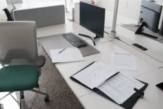 Ilustrasi: Meja kerja kantor modern dengan monitor komputer, berkas dokumen, dan kursi kerja.