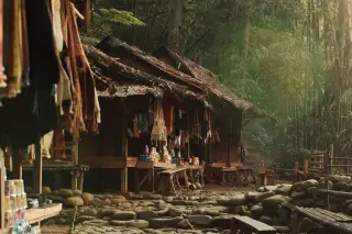 Ilustrasi: Deretan warung tradisional beratap jerami di jalan berbatu dekat hutan bambu.
