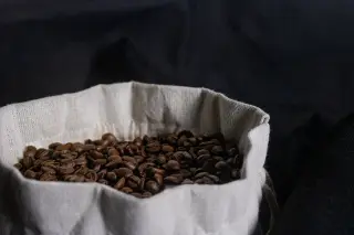 Ilustrasi: Biji kopi sangrai di dalam kantong kain putih dengan latar belakang hitam.