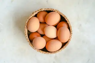 Ilustrasi: Tampilan dari atas sejumlah telur ayam cokelat di dalam keranjang anyaman kecil di atas meja marmer.