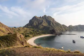Ilustrasi: Pemandangan bukit dan pantai di Pulau Padar dengan kapal wisata di perairan.