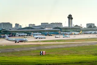 Ilustrasi: Pesawat-pesawat komersial di apron bandara dengan latar terminal modern dan menara pengawas.
