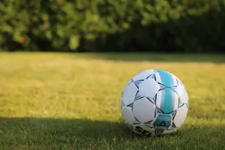 Ilustrasi: Sebuah bola sepak berwarna putih dan biru tergeletak di atas rumput hijau.