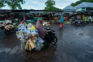 Ilustrasi: Seorang wanita mengendarai sepeda motor bermuatan dagangan di area pasar terbuka.