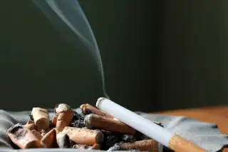 Ilustrasi: Sebatang rokok menyala di atas asbak berisi puntung rokok.