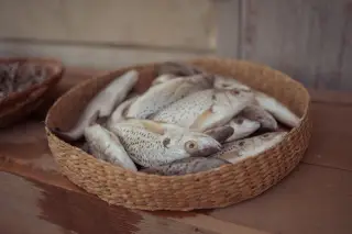 Ilustrasi: Beberapa ekor ikan segar diletakkan di dalam wadah anyaman di atas meja kayu.