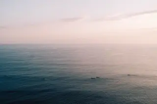 Ilustrasi: Pemandangan laut luas yang tenang dengan beberapa perahu kecil berlayar di kejauhan saat fajar.