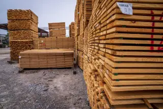 Ilustrasi: Tumpukan papan kayu yang tersusun rapi di area penyimpanan terbuka.