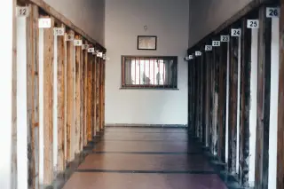 Ilustrasi: Lorong bangunan kosong dengan tiang bernomor di sisinya dan jendela berterali di ujungnya.