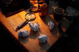 Ilustrasi: Kaca pembesar, gumpalan kertas, dan secarik surat di atas meja kayu dengan pencahayaan hangat.