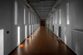 Ilustrasi: Lorong bangunan kosong yang panjang dengan lantai cokelat dan dinding putih berderet jendela.