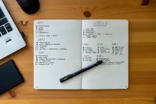 Ilustrasi: Buku catatan terbuka dengan pena di atas meja kayu di sebelah laptop.
