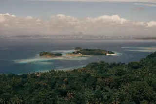 Ilustrasi: Pemandangan pulau-pulau kecil di tengah laut berlatar garis pantai berhutan dan langit berawan.
