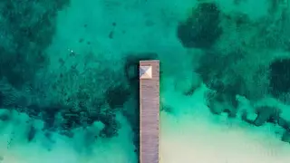 Ilustrasi: Pemandangan udara dermaga kayu yang menjorok ke perairan laut jernih berwarna toska.