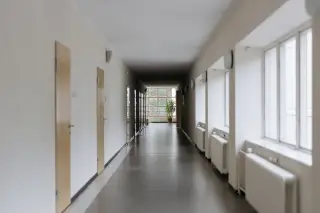 Ilustrasi: Lorong panjang yang sepi di dalam gedung dengan deretan pintu dan jendela besar.
