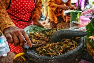 Ilustrasi: Seseorang mengulek sayuran berbumbu di atas cobek batu besar di sebuah warung.