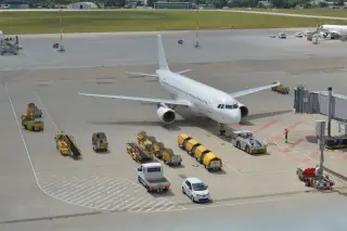 Ilustrasi: Pesawat komersial putih parkir di apron bandara dikelilingi kendaraan operasional.