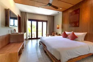 Ilustrasi: Interior kamar hotel yang rapi dengan tempat tidur besar dan pintu kaca menuju teras luar.