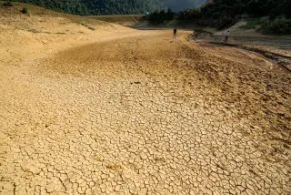 Ilustrasi: Hamparan tanah dasar sungai yang retak-retak kering dengan dua orang berjalan di kejauhan.