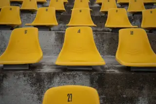 Ilustrasi: Deretan kursi stadion berwarna kuning terpasang pada tribun beton bertingkat.