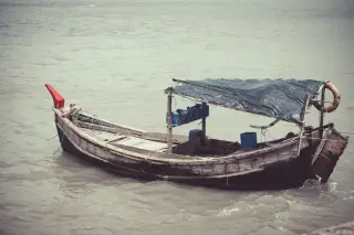 Ilustrasi: Sebuah perahu kayu tradisional bertenda terombang-ambing di atas air laut yang tenang.