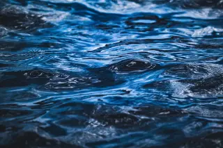 Ilustrasi: Foto jarak dekat tekstur permukaan air laut berwarna biru dengan riak gelombang.
