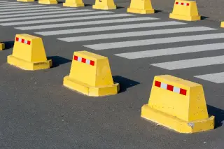 Ilustrasi: Pembatas jalan kuning berjajar di aspal dekat garis zebra cross.