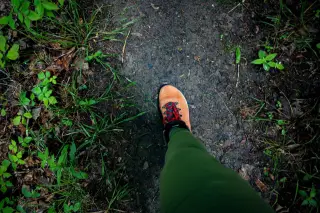 Ilustrasi: Kaki seseorang bersepatu bot mendaki melangkah di atas jalan setapak tanah.