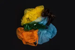 Ilustrasi: Komposisi kantong plastik warna-warni dan botol plastik remuk di atas latar belakang hitam.
