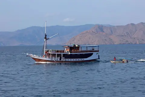 Ilustrasi: Sebuah kapal wisata berlayar di laut dengan latar belakang bukit gersang.