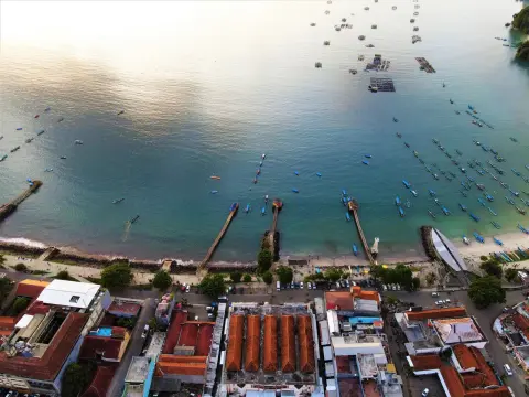Ilustrasi: Pemandangan udara kawasan pesisir pantai dengan dermaga kecil, jejeran perahu, dan deretan bangunan.