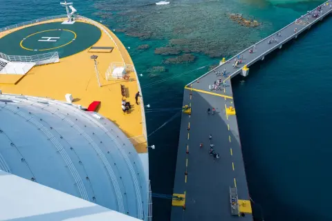 Ilustrasi: Pemandangan dari atas sebuah kapal penumpang besar yang bersandar di dermaga panjang di laut biru.
