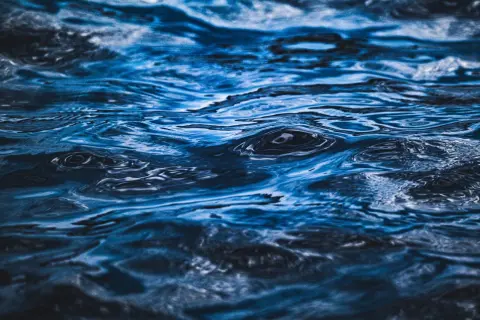 Ilustrasi: Foto jarak dekat tekstur permukaan air laut berwarna biru dengan riak gelombang.